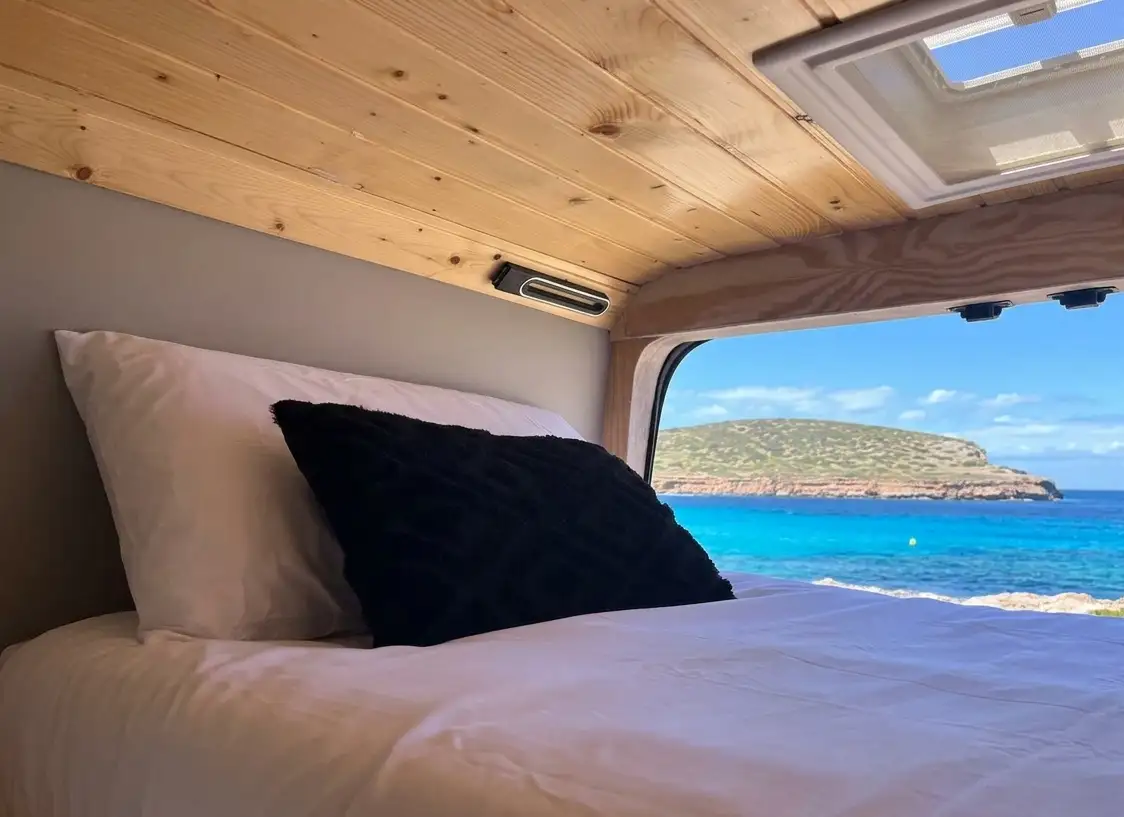 Cama litera individual superior en camper Hyundai H350 con ventana y vistas a Cala Comte.